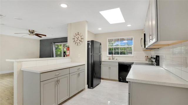 88 Valencia Dr, Ormond Beach, FL 32176 - kitchen with black appliances, a sink, a skylight, backsplash, and light stone counters