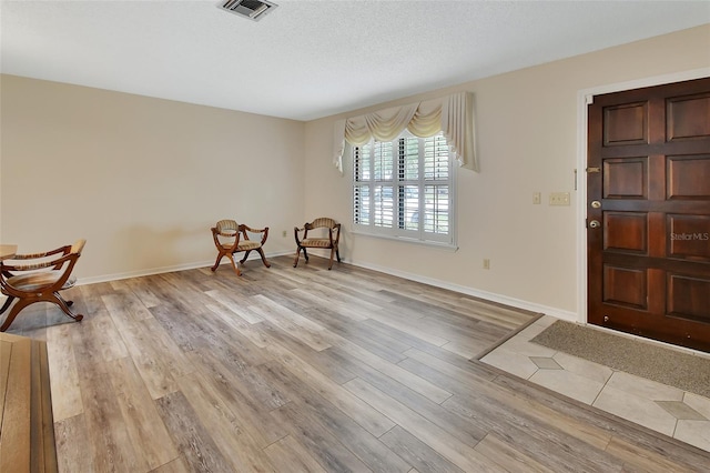 unfurnished room with a textured ceiling, baseboards, visible vents, and light wood finished floors
