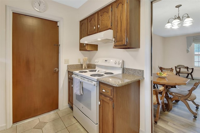 kitchen with an inviting chandelier, under cabinet range hood, white range with electric stovetop, brown cabinets, and light stone counters
