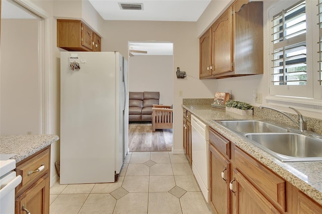 kitchen with brown cabinets, light tile patterned flooring, a sink, white appliances, and visible vents