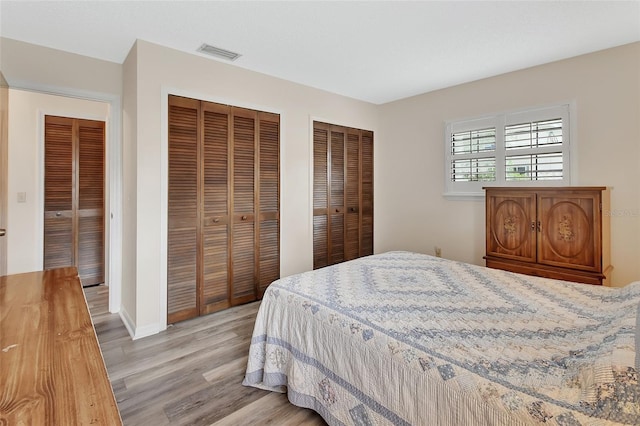 bedroom featuring multiple closets, baseboards, light wood finished floors, and visible vents