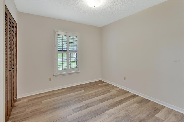 spare room with baseboards, a textured ceiling, and light wood finished floors