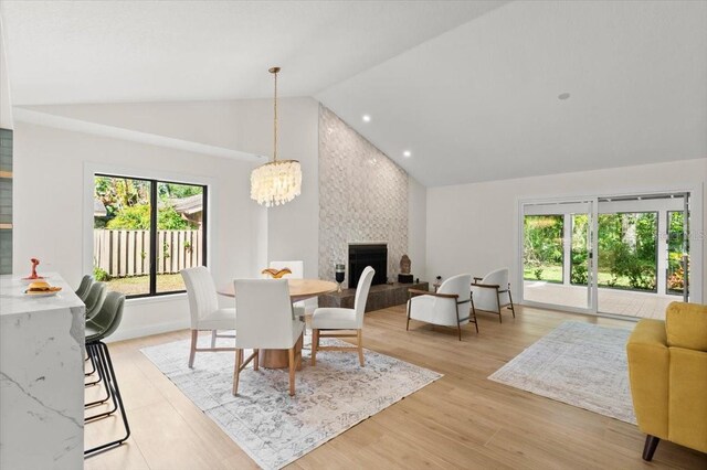 dining space featuring a large fireplace, high vaulted ceiling, a notable chandelier, and plenty of natural light