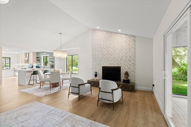 living area with plenty of natural light, a notable chandelier, light wood-type flooring, and lofted ceiling