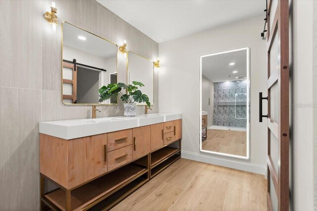 full bath with double vanity, a shower stall, wood finished floors, a sink, and recessed lighting