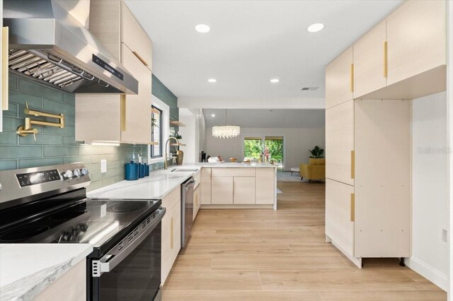 kitchen with appliances with stainless steel finishes, a sink, light wood finished floors, a peninsula, and wall chimney exhaust hood