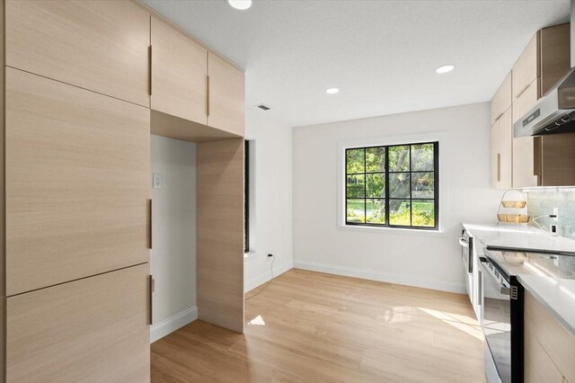 kitchen with light countertops, baseboards, wall chimney range hood, and dishwasher
