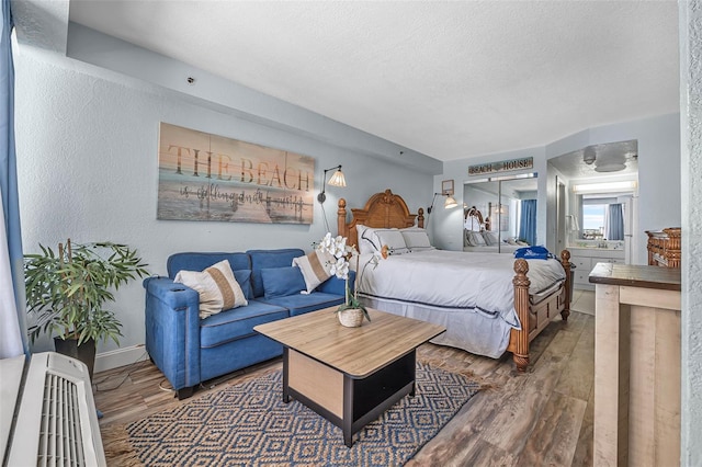 bedroom featuring baseboards, a textured ceiling, a textured wall, and wood finished floors