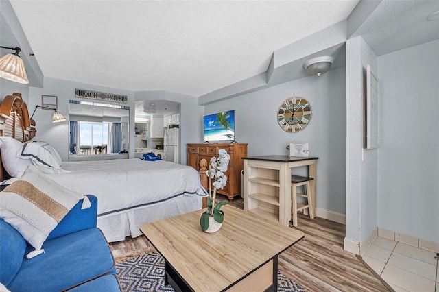 bedroom featuring baseboards, freestanding refrigerator, and light wood-type flooring