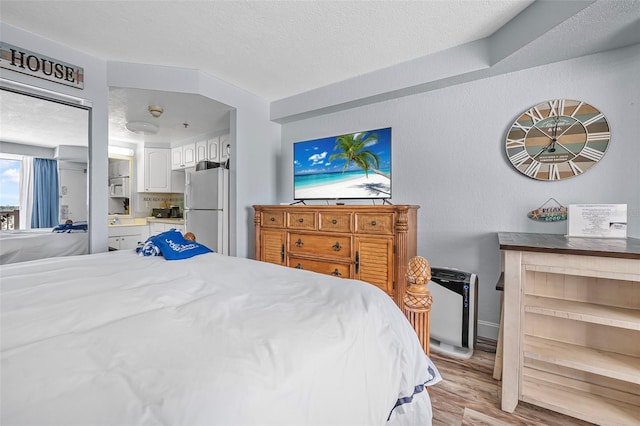 bedroom featuring freestanding refrigerator, light wood finished floors, and a textured ceiling