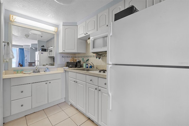 kitchen with white appliances, a textured ceiling, white cabinetry, a sink, and light tile patterned floors