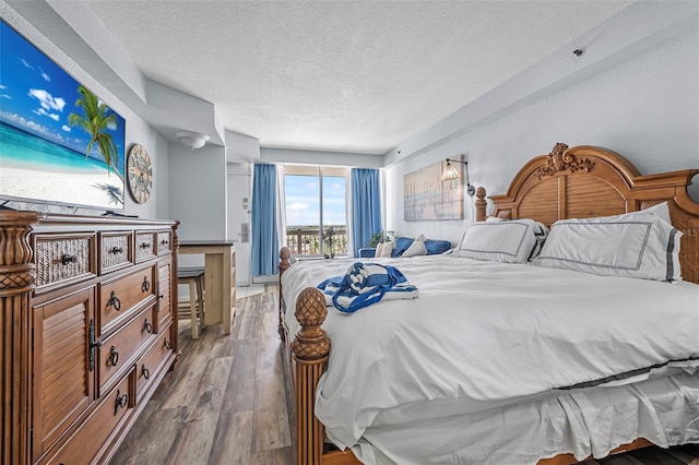 bedroom with a textured ceiling, wood finished floors, and access to exterior