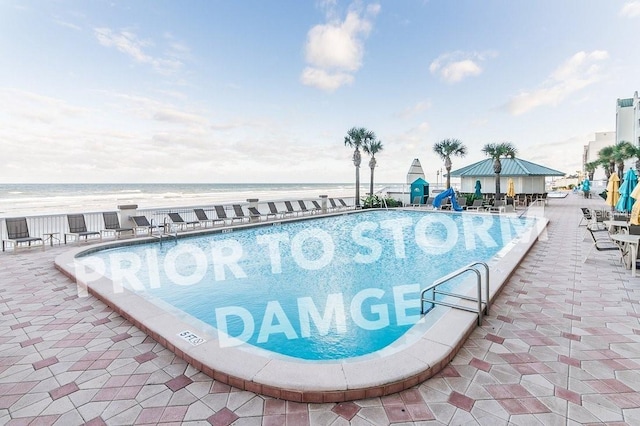 pool featuring a view of the beach, a water view, and a patio area