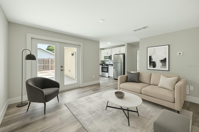living room featuring french doors, light wood-type flooring, visible vents, and baseboards