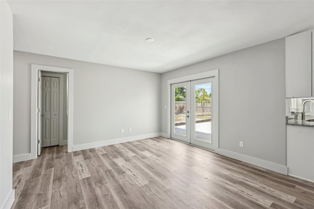 empty room with baseboards, french doors, and light wood-type flooring