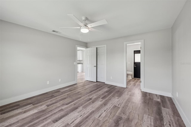 unfurnished bedroom with a ceiling fan, baseboards, visible vents, connected bathroom, and wood finished floors