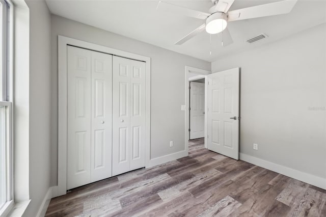unfurnished bedroom with a closet, visible vents, wood finished floors, and baseboards