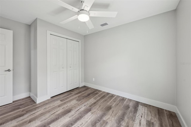 unfurnished bedroom featuring wood finished floors, a closet, visible vents, baseboards, and ceiling fan