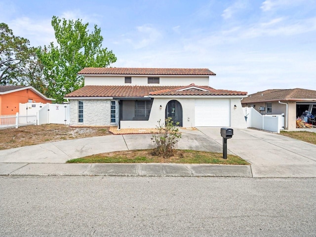 mediterranean / spanish-style home with a gate, stucco siding, a tiled roof, and concrete driveway
