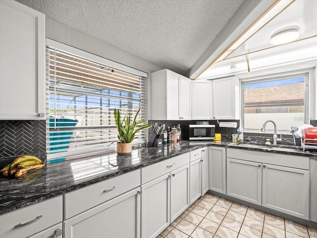 kitchen featuring a sink, stainless steel microwave, backsplash, and a textured ceiling