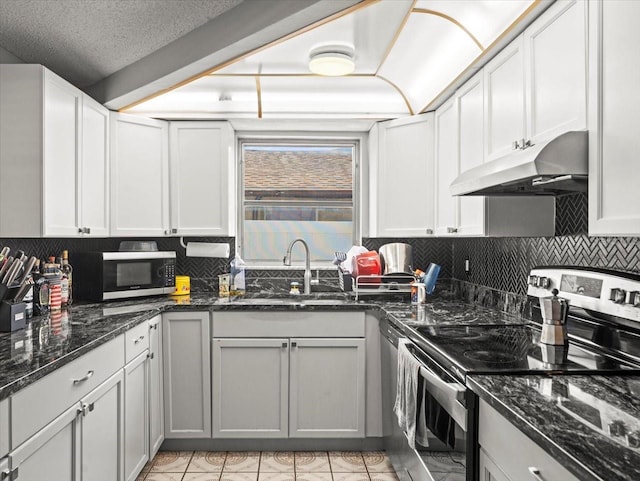 kitchen with backsplash, appliances with stainless steel finishes, a sink, dark stone countertops, and under cabinet range hood