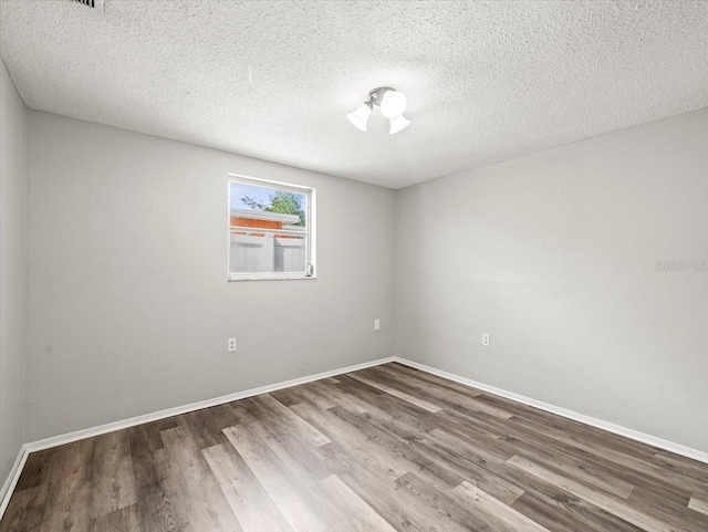 empty room with baseboards, a textured ceiling, and wood finished floors