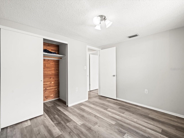 unfurnished bedroom featuring a textured ceiling, baseboards, wood finished floors, visible vents, and a closet