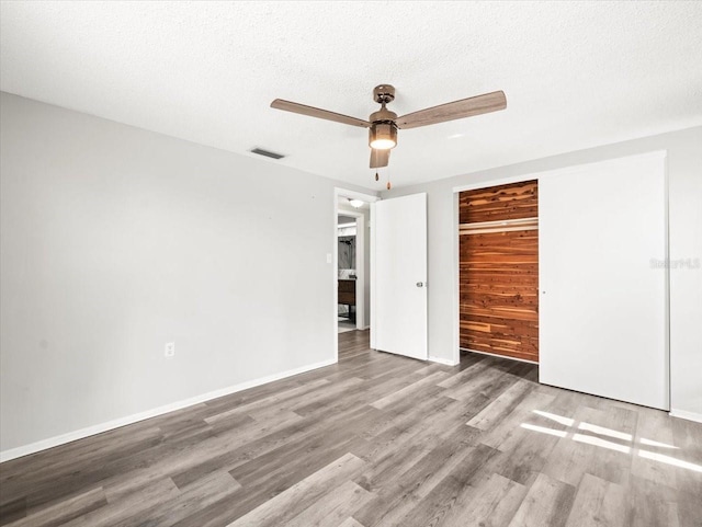 unfurnished bedroom with a closet, visible vents, wood finished floors, baseboards, and a ceiling fan