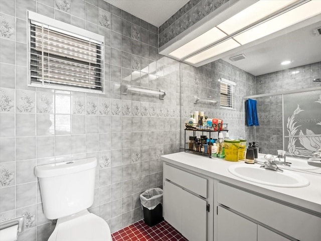 bathroom featuring visible vents, tile walls, a tile shower, vanity, and toilet