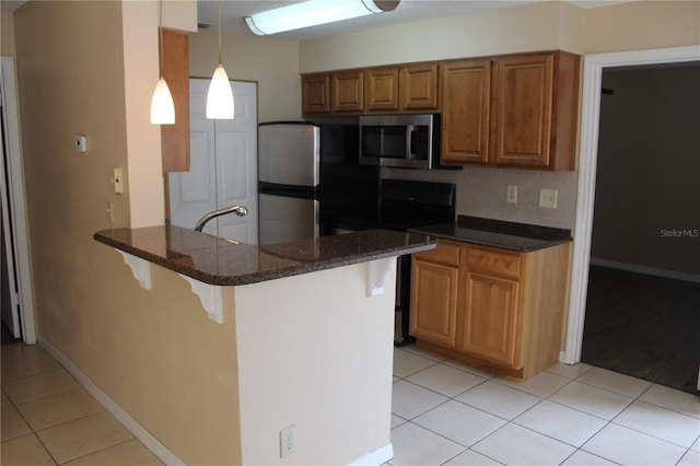 kitchen with brown cabinets, appliances with stainless steel finishes, a kitchen breakfast bar, a peninsula, and light tile patterned floors