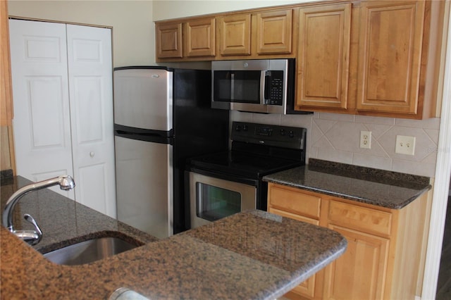 kitchen featuring a sink, appliances with stainless steel finishes, backsplash, and dark stone countertops