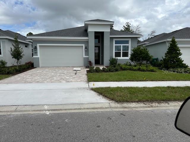 prairie-style home featuring a garage, stucco siding, decorative driveway, and a front yard
