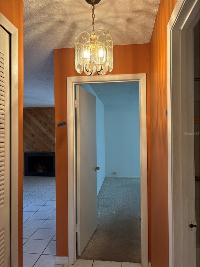 corridor featuring a chandelier, a textured ceiling, tile patterned flooring, and wooden walls