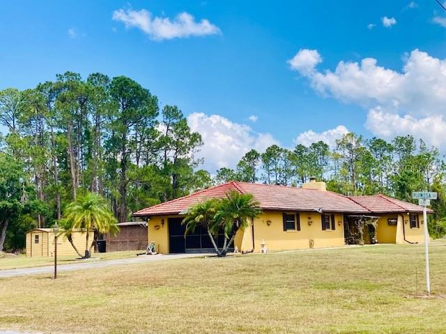 back of house with an outdoor structure, a storage unit, a yard, concrete driveway, and stucco siding
