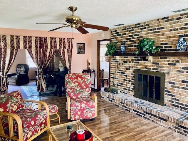 living area featuring a textured ceiling, a fireplace, a ceiling fan, and wood finished floors