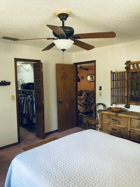 bedroom with ceiling fan, a textured ceiling, baseboards, a spacious closet, and a closet