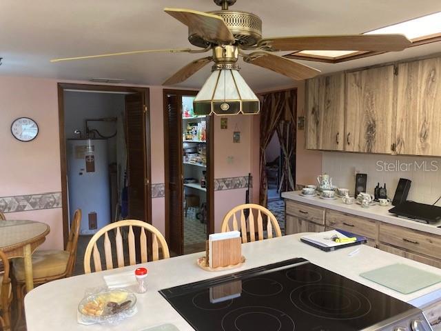 kitchen with electric range oven, light countertops, brown cabinetry, water heater, and a ceiling fan