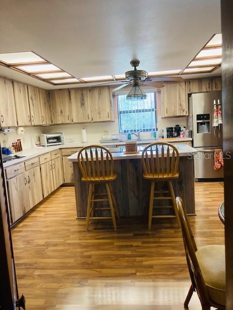 kitchen with stainless steel fridge, light brown cabinetry, light wood-style floors, and a breakfast bar area
