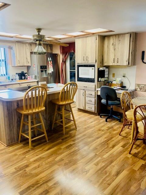 kitchen with light brown cabinetry, stainless steel fridge with ice dispenser, light wood-style floors, light countertops, and a kitchen breakfast bar