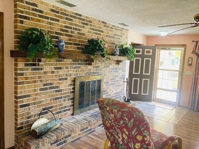 interior space with visible vents, a textured ceiling, a brick fireplace, and wood finished floors