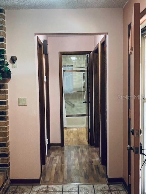 corridor featuring a textured ceiling, baseboards, and wood finished floors