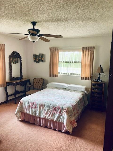carpeted bedroom with a ceiling fan and a textured ceiling