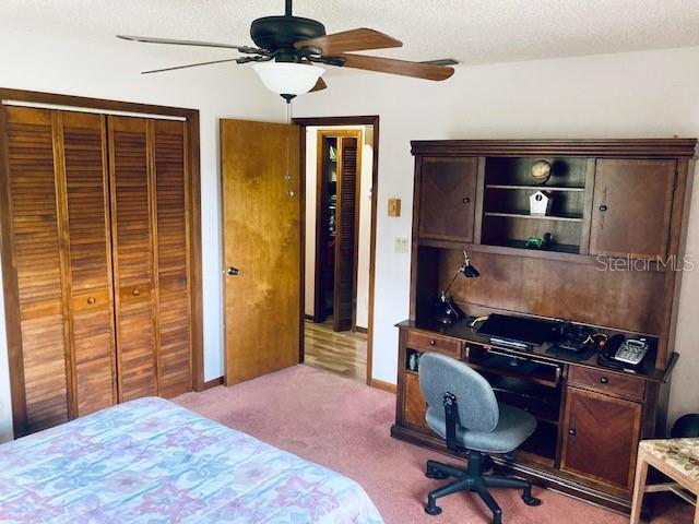 carpeted bedroom with a textured ceiling, ceiling fan, and a closet