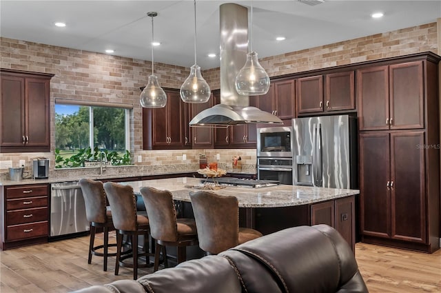 kitchen with decorative backsplash, island range hood, a sink, a breakfast bar, and stainless steel appliances
