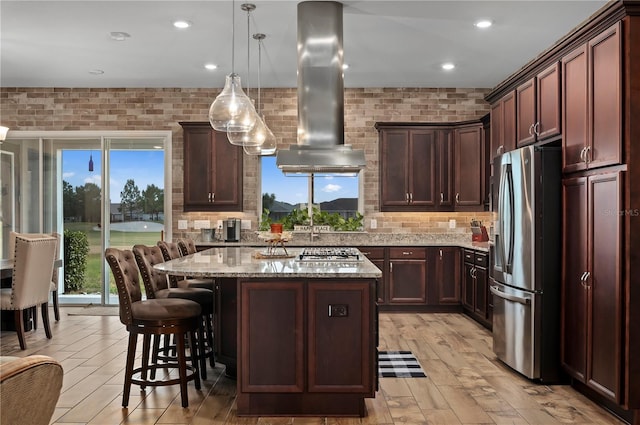 kitchen featuring a kitchen breakfast bar, a kitchen island, light stone counters, stainless steel appliances, and extractor fan