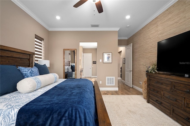 bedroom featuring crown molding, an accent wall, baseboards, wood finished floors, and visible vents