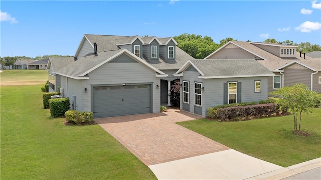 view of front of home featuring roof with shingles, decorative driveway, a front yard, and a garage
