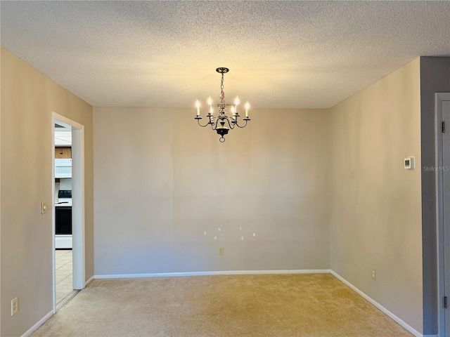 spare room featuring light colored carpet, a textured ceiling, baseboards, and a notable chandelier