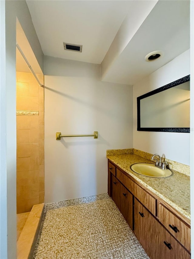 bathroom featuring a tile shower, vanity, and visible vents