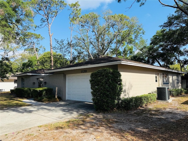 view of side of home featuring central air condition unit, a garage, driveway, and brick siding